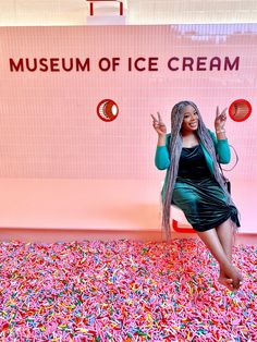 a woman with long hair standing in front of a museum ice cream sign surrounded by sprinkles