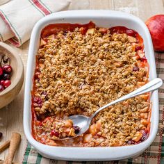 an apple cranberry crisp in a white casserole dish with a spoon