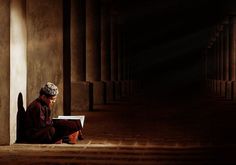 a man sitting on the floor reading a book in an empty room with columns and pillars