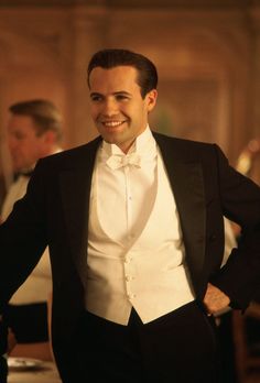 a man in a tuxedo smiles as he stands with his hands on his hips