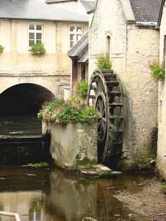 an old water mill with flowers growing out of it