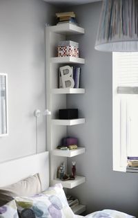 a white bed sitting under a window next to a lamp on top of a book shelf