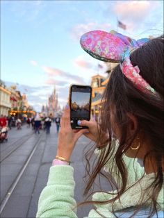 a woman taking a photo with her cell phone in front of the disney mouse ears