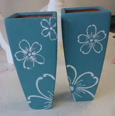 two blue vases with white flowers painted on them sitting on a table next to each other