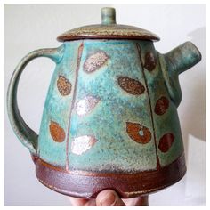 a hand holding a ceramic teapot with leaves on it