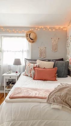 a white bed topped with lots of pillows next to a window covered in string lights