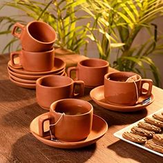 a table topped with lots of brown cups and saucers next to cookies on plates