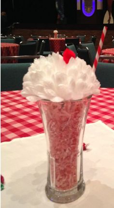 a cup filled with candy and whipped cream on top of a table covered in red and white checkered cloth