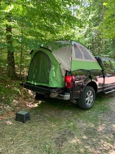 a truck is parked in the woods with a tent attached to it's back