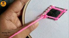 a person holding a pink toothbrush in front of a piece of fabric with beads on it