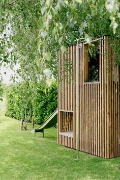 a wooden play structure in the middle of a grassy area with a slide and tree