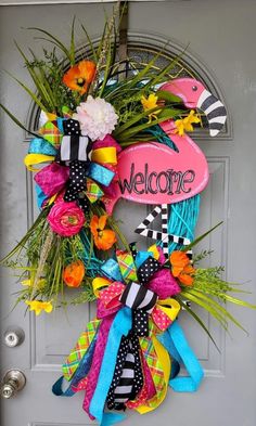 a colorful welcome wreath with flowers and ribbons hanging on the front door for someone's house