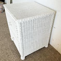 a white wicker storage box sitting on the floor next to a wall and carpet