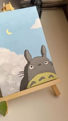 an easel with a painting of a totoro in the sky on it