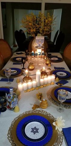 the table is set with candles and plates for hanukkah dinner guests to enjoy