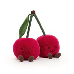 two stuffed cherries sitting next to each other on a white surface with one holding a green leaf