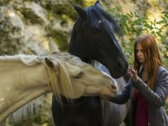 two women petting horses in front of some rocks and trees, while another woman holds her hand out to touch the horse's face