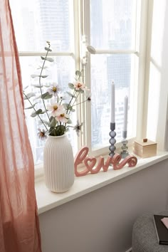 a vase filled with flowers sitting on top of a window sill next to two candles