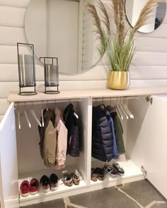 a white shelf with clothes and shoes on it in front of a round mirror, next to a potted plant