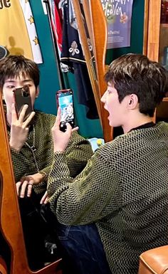 two young men sitting in front of a mirror while looking at their cell phones and taking pictures