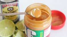 a jar of peanut butter with a spoon in it and some limes next to it