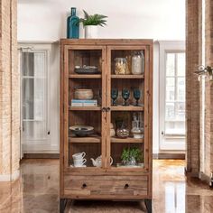 a wooden cabinet with glass doors in the middle of a room next to a brick wall