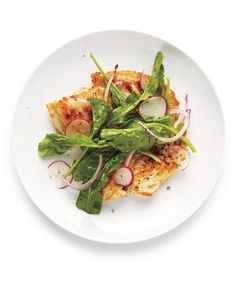 a white plate topped with meat and veggies on top of a green leafy salad