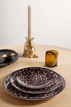 the table is set with black and gold plates, candlesticks and an animal print plate