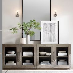 a large mirror sitting on top of a wooden cabinet next to a vase and plant