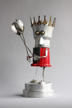 a silver and red robot holding two spoons on top of it's head