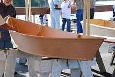 two men working on a wooden boat in a workshop with other people standing around and looking at it