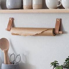 some cups and spoons are hanging on the wall next to a shelf with utensils