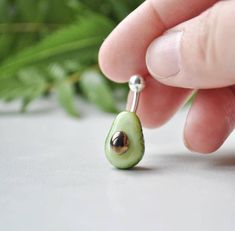 a person is holding an avocado dangling from a tiny hook - on earring