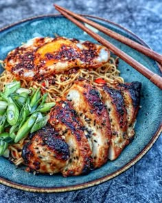 a blue plate topped with meat and noodles next to chopsticks on a table