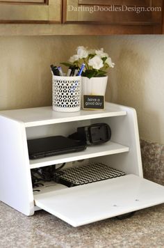 a white shelf with some electronics on it and flowers in a vase next to it