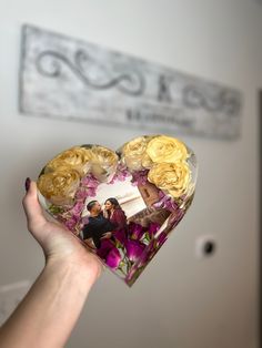 a person holding a heart shaped box filled with flowers and miniature figurines in it