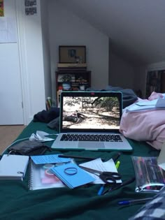 an open laptop computer sitting on top of a green bed covered in books and papers