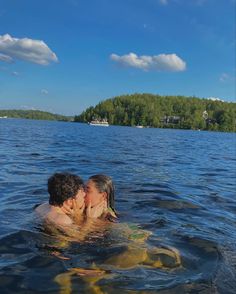 two people are kissing in the water on a sunny day with trees in the background