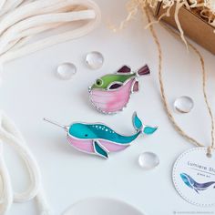 two colorful fish earrings sitting on top of a white table next to a cup and saucer