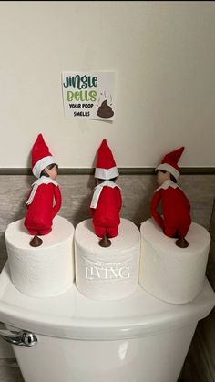 three elfs are sitting on top of two rolls of toilet paper in the bathroom