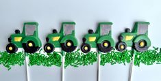 a row of green tractor cupcakes on top of white cake sticks with grass