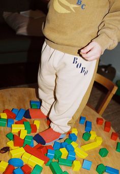 a toddler standing on top of a wooden table surrounded by colorful plastic blocks and letters