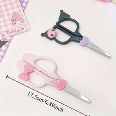 two pairs of scissors with pink and black handles are on a table next to a notepad