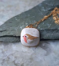 a necklace with a bird painted on it sitting on a rock next to a chain