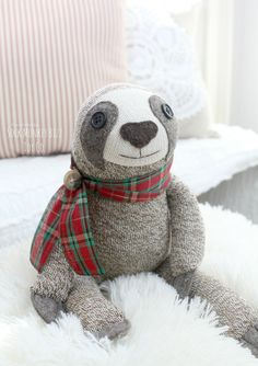 a stuffed slotty bear wearing a scarf and sitting on a fluffy white bed sheet