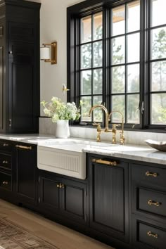 a kitchen with black cabinets and white counter tops, gold faucets and brass pulls