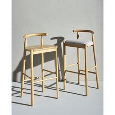 two wooden stools sitting next to each other in front of a gray wall with shadows on the floor