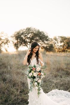 a woman in a wedding dress is holding a bouquet and posing for the camera with her hands behind her head