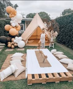 a tent set up with balloons and pillows on the ground in front of some trees