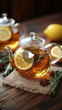 a glass teapot filled with lemon slices and herbs on top of a wooden table